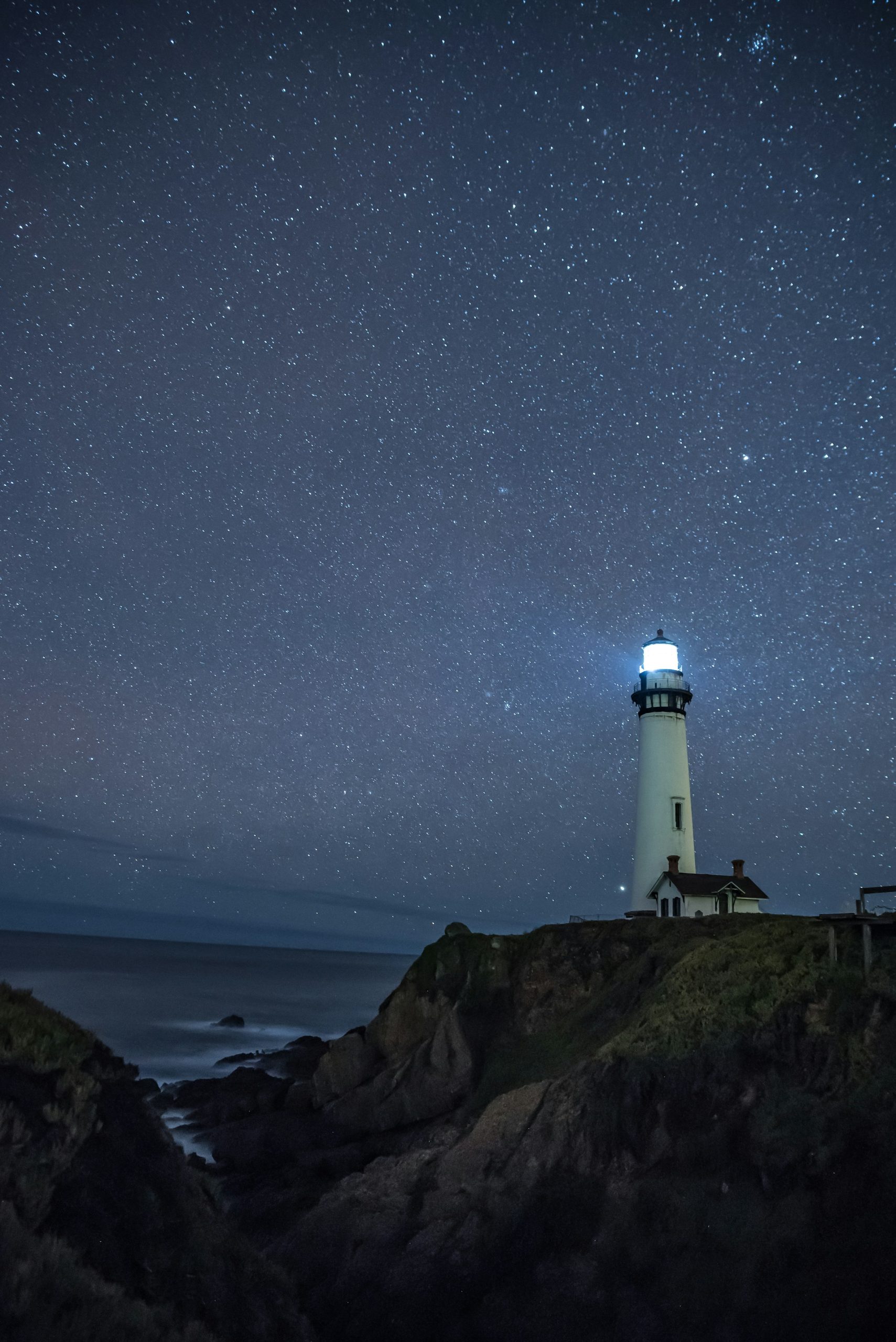 A lit lighthouse standing out against a vast, star-filled night sky